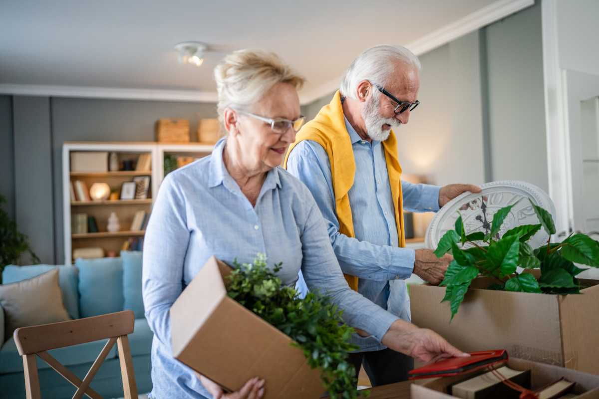 family senior couple man woman husband and wife pensioner grandfather grandmother moving in new apartment taking their stuff belongings and plants in or out of boxes packing or unpacking real people