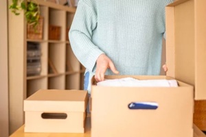 woman unpacking clothes from a cardboard box after moving into a new house